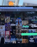 A laptop screen displays a web page featuring a mix of movie and TV show covers, highlighting popular titles and a Hulu and Disney+ bundle promotion. There are visible icons and images of films and shows alongside promotional text offering entertainment and live sports.
