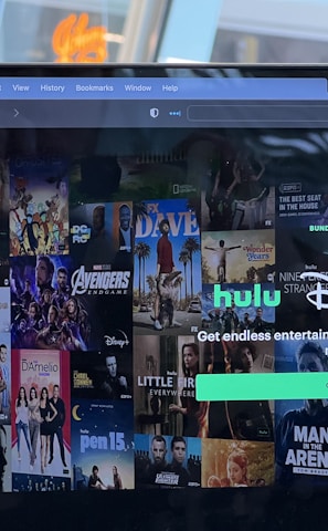 A laptop screen displays a web page featuring a mix of movie and TV show covers, highlighting popular titles and a Hulu and Disney+ bundle promotion. There are visible icons and images of films and shows alongside promotional text offering entertainment and live sports.